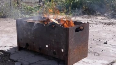Açık havada dumanlı odun sobasında parlak bir alevle doğranmış odun yanığı. Kızgın kırmızı bir şenlik ateşi, durgun bir ızgarada, güneş ışığının arka bahçesinde beton asfalt üzerinde duruyor..