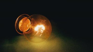 Sarı parlak lamba yanıyor, Flickers in a Green Background in Dark Room. Kapatın. Tungsten ampulü, yanıp sönen sıcak ışık titreşimleriyle masada yatıyor. Elektrik kesintisi, elektrik kesintisi. Kriz.