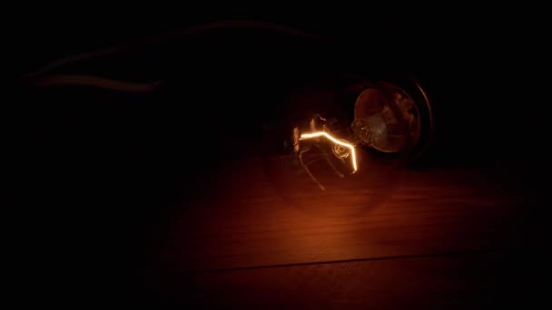 古い白熱灯が点灯し 暗い部屋の木製の背景にフリッカー 閉めろ 暖かい点滅光脈動を持つワイヤ上のタングステン電球は テーブルの上にあります — ストック動画