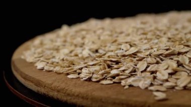 Siyah Dönen Arkaplanda Yulaf Ezmesi Yığını İçinde Düşen Kuru Yulaf Gevreği. Makro. Kapatın. Doku tahılı. Tahta tabak. Sağlıklı diyet kahvaltısı. Faydalı yemek. Fast food. Mısır, tahıl, buğday. Boşluğu kopyala.