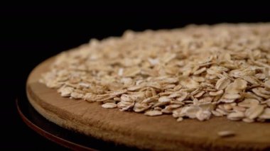 Yaklaş, Kuru Yulaf Gevrekleri Kara Arkaplanda Tahta Tabakta Yavaşça Döndür. Yan görüş. Mesaj için yer var. Doku. Makro. Dön. Bir yığın çiğ yulaf ezmesi. Sağlıklı diyet kahvaltısı. Faydalı yemek..