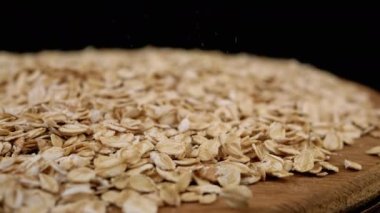 Siyah Dönen Arkaplanda Yulaf Ezmesi Yığını İçinde Düşen Kuru Yulaf Gevreği. Makro. Kapatın. Doku tahılı. Tahta tabak. Sağlıklı diyet kahvaltısı. Faydalı yemek. Fast food. Mısır, tahıl, buğday. Boşluğu kopyala.