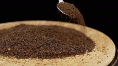 El, Yüzeydeki Çay Yığını Üzerine Bir Kaşıktan Dökülen Kurutulmuş Kara Çay Yaprakları. Siyah arka plan. Uzayı kopyala Kuru çay bolluğu. Şifalı bitki. Hareket. İçelim. Soyut. Doku. Tahta tabak..