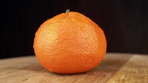 黒い背景を回転させると 水が単一の熟したオレンジに落ちます 新鮮なオレンジの果実 木製の板の上で回転する 隔離されてる 明るいタンジェリン 水の粒子 スローモーション 閉じろ — ストック動画