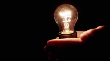 Elleri Tutan Kişi, Karanlık Oda 'daki Edison Ampulü' nü de içeriyor. Sıcak ışıklı Tungsten akkor ampulü. Enerji krizi. Siyah arka plan. Elektrik, lambanın ısıtması..