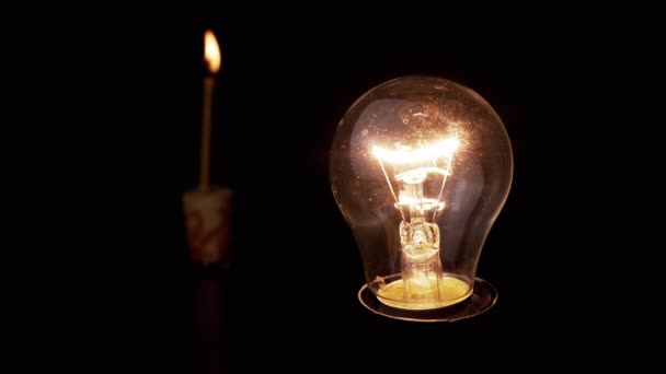 在燃烧的蜡烛的黑色背景的黑暗房间里发光灯泡 爱迪生把白炽灯泡上的炽热灯打开了 能源危机 停电了 停电了走吧 — 图库视频影像