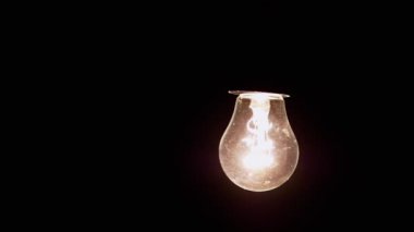Sallanan Parlayan Edison Parlayan Ampulü Siyah Arkaplanda Asmak. Eski bir Edison tungsten ampulü karanlıkta parlıyor. Sıcak sarı ışık. Yapı, toz. Rahat, rahat bir konsept..