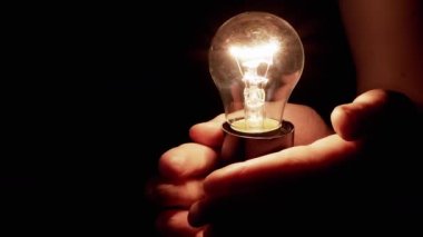 Elleri Tutan Kişi, Karanlık Oda 'daki Edison Ampulü' nü de içeriyor. Sıcak ışıklı Tungsten akkor ampulü. Enerji krizi. Siyah arka plan. Elektrik, lambanın ısıtması..