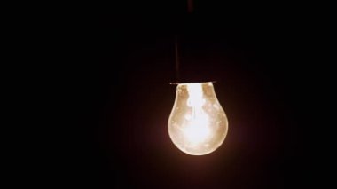 Kara Arkaplan 'daki Karanlık Oda' da sallanan titreşimli ampul. Yaşlı Edison tungsten parlıyor ve kapanıyor. Enerji krizi. Elektrik var. Elektrik kesintisi. Kesinti. Değiştir.