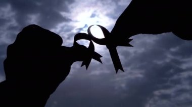 Gri Bulutların Arkasında İki Pembe Kurdele Gösteren Kadın Elleri 'nin Silueti. Göğüs kanseri sembolü olan bir el penceredeki kümülüs bulutları arasından güneş ışığına ulaşır. Ekim ayı.