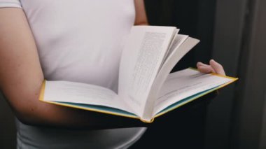 Yaklaş, Tanınmayan Çocuk Bir Kitabın Sayfalarını karıştırıyor. Ayakta duran, elinde bir kitap tutan, yavaşça sayfaları çeviren biri. Okuyorum. Arka plan bulanık. Eğitim kavramı.