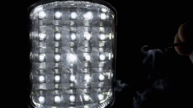 Parlayan Led Flashlight 'ın Siyah Arkaplanında Yanan Kibriti Erkek Üflüyor. Duman ve duman dokusunun hareketi. Enerji krizi kavramı, bilinç kaybı, enerji tasarrufu. Soyut. Boşluğu kopyala.