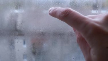Kadın Elleri Islak Bir Pencerede Parmaklarla Çizim Yapıyor. Aşkın kalp sembolü. Yoğunlaşan damlalar camdan aşağı akıyor. Sevdiğinin hasretini çekiyorsun. Evde izole edilmiş. Kasvetli yağmurlu bir gün.