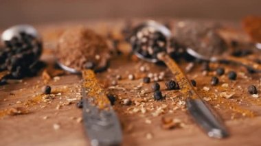 Yakın plan, Hint Baharatlı Kaşıklar Renkli Tahta Arkaplanda Dönüyor. Ağır çekim. Dağıtılmış baharat karışımı, karabiber, zerdeçal, paprika, kişniş, kekik. Arkaplan, doku.
