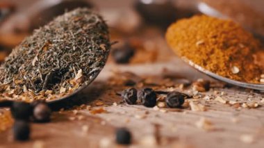 Yakın plan, Hint Baharatlı Kaşıklar Renkli Tahta Arkaplanda Dönüyor. Ağır çekim. Dağıtılmış baharat karışımı, karabiber, zerdeçal, paprika, kişniş, kekik. Arkaplan, doku.