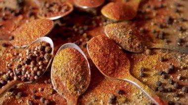 Hint baharatlı kaşıklar renkli ahşap arka planda döner. Kapatın. Ağır çekim. Dağıtılmış baharat karışımı, karabiber, zerdeçal, paprika, kişniş, kekik. Arkaplan, doku.
