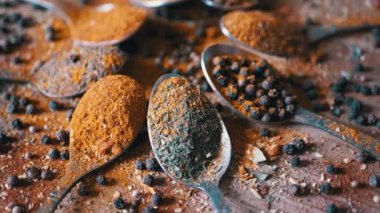 Hint baharatlı kaşıklar renkli ahşap arka planda döner. Kapatın. Ağır çekim. Dağıtılmış baharat karışımı, karabiber, zerdeçal, paprika, kişniş, kekik. Arkaplan, doku.