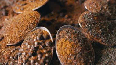 Yakın plan, Hint Baharatlı Kaşıklar Renkli Tahta Arkaplanda Dönüyor. Ağır çekim. Dağıtılmış baharat karışımı, karabiber, zerdeçal, paprika, kişniş, kekik. Arkaplan, doku.
