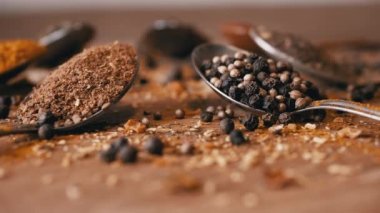 Yakın plan, Hint Baharatlı Kaşıklar Renkli Tahta Arkaplanda Dönüyor. Ağır çekim. Dağıtılmış baharat karışımı, karabiber, zerdeçal, paprika, kişniş, kekik. Arkaplan, doku.