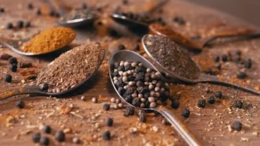 Yakın plan, Hint Baharatlı Kaşıklar Renkli Tahta Arkaplanda Dönüyor. Ağır çekim. Dağıtılmış baharat karışımı, karabiber, zerdeçal, paprika, kişniş, kekik. Arkaplan, doku.