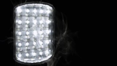 Parlayan El fenerinin Siyah Arkaplanında Bir Duman Bulutu Yükseliyor. Duman dokusu. Enerji krizi kavramı, bilinç kaybı, enerji tasarrufu. Soyut. Ampullü spot ışığı. Bulanık arkaplan.