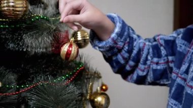 Yaklaş, Çocuk Elleri Noel Ağacı 'nı Parlak Altın Toplarla süsle. Ağacın dalındaki oyuncak. Noel süsü. Mutlu aile kavramı. Noel süsü, dekorasyon, ev dekorasyonu. Xmas. Tatil.