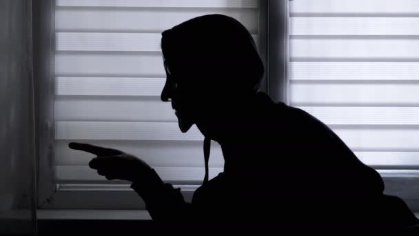 一个戴着面具的无法辨认的人的肖像在窗边展示着一个拳头 挑衅的姿态 挥动拳头侧视图 一个戴头巾的男人的特征 黑暗的房间暗影游戏被隔离了 — 图库视频影像