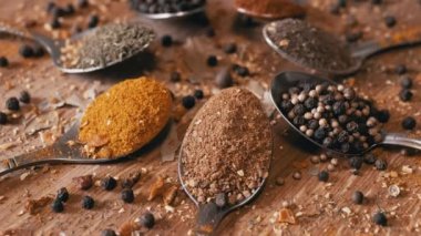 Yakın plan, Hint Baharatlı Kaşıklar Renkli Tahta Arkaplanda Dönüyor. Ağır çekim. Dağıtılmış baharat karışımı, karabiber, zerdeçal, paprika, kişniş, kekik. Arkaplan, doku.