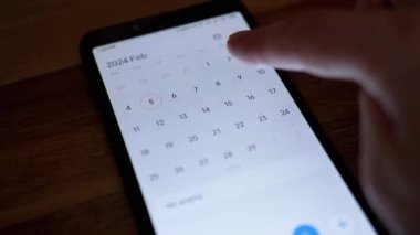 Kız, Smartphone Screen 'de Elektronik Takvim Uygulamasına Yeni Bir Olay Ekliyor. İstenen tarihi bulmak için elektronik sayfayı elle çevirir. Başvuruya bir olay ekleniyor. Sevgililer Günü.