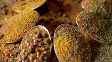 Yakın plan, Hint Baharatlı Kaşıklar Renkli Tahta Arkaplanda Dönüyor. Ağır çekim. Dağıtılmış baharat karışımı, karabiber, zerdeçal, paprika, kişniş, kekik. Arkaplan, doku.