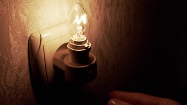 手は光る電球をオフにし 夜の光は壁のソケットに挿入されます 閉めろ 暗い部屋のキャンドルの形でタングステンフィラメントランプ 寝る時間だ 屋内だ 電力を節約する — ストック動画