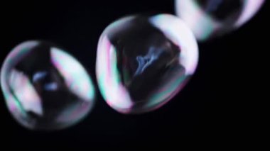 Renkli sabun köpükleri izole edilmiş siyah arka planda boş bir alanda uçuyor. Birçok gökkuşağı şeffaf kabarcıkları rastgele döner, yüzer, düşer. Bulanık hareket. Seçici odaklanma. Soyut. Oyun bitti. Yavaş çekim.