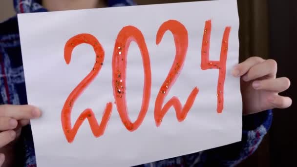 近视时 手握一张印有2024年绘画日期的专辑单张 横幅上刻有2024年的字用红漆涂上了菱形石 新年在家里 — 图库视频影像