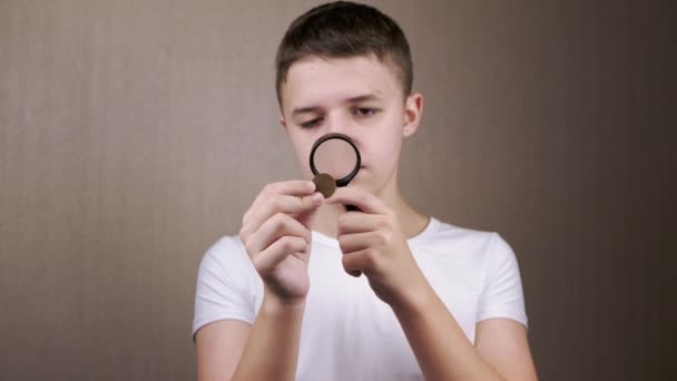 近距离观察 青少年通过放大镜检查发现的旧硬币 好奇的男孩喜欢数字学 身体的一部分 模糊的背景 年轻的钱币学家看着符号符号数字Hobby — 图库视频影像