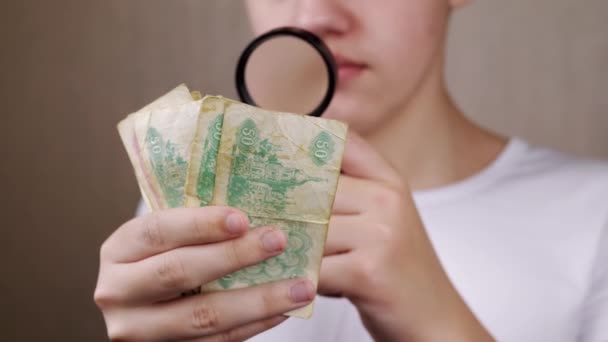 青少年通过放大镜检查乌克兰旧币 靠近点严重好奇的男孩看着标志 钞票上的数字 Hobby 灰色模糊的背景 收集资料 — 图库视频影像