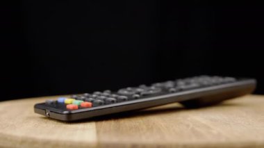 Kapatın, TV Uzaktan Kumandası Kara Arkaplanda Tahta üzerinde Dönüyor. Yan görüş. Bulanık hareket. Seçici odaklanma. Dön. Dönüp duruyoruz. Döngü. Uzayı kopyala Mesaj için yer. İzole edilmiş. Düğmeler.