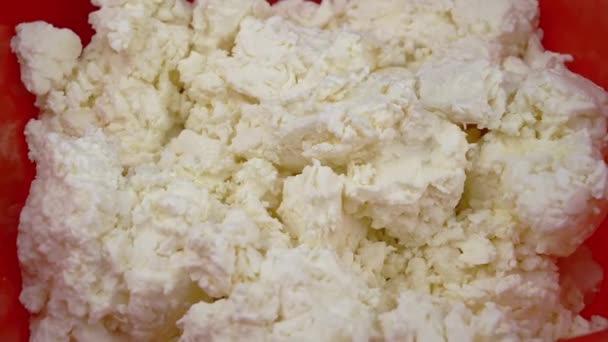 回転する背景に赤いプラスチック製のボウルに白いコテージチーズのテクスチャ 閉めろ 黄色の色合いの脂肪質の新鮮なコテージチーズの表面 赤ちゃん用 健康的な有機食品 — ストック動画