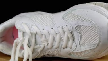 Bir çift beyaz deri spor ayakkabı, siyah arka planda, karton bir kutuda dönüyor. Kapatın. Bağcıklar, ağ, delikler, kumaş yapısı. Yan görüş. Seçici odaklanma. Tepeden tırnağa. Kadın ayakkabıları. Fitness. Spor..