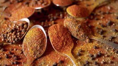 Hint baharatlı kaşıklar renkli ahşap arka planda döner. Kapatın. Ağır çekim. Dağıtılmış baharat karışımı, karabiber, zerdeçal, paprika, kişniş, kekik. Arkaplan, doku.