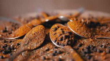 Hint baharatlı kaşıklar renkli ahşap arka planda döner. Kapatın. Ağır çekim. Dağıtılmış baharat karışımı, karabiber, zerdeçal, paprika, kişniş, kekik. Arkaplan, doku.