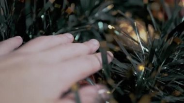 Yumuşak bir çelenk içinde Kadın El Dokunuşu Gizli Noel Oyuncakları. Noel arkaplanı. Kapatın. Kaygan eller. Kamera hareketi. Yakın plan. Doku. Noel süsleri. Olumlu duygular. Hissetmek.