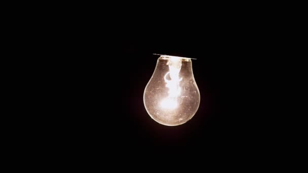 ブラックを背景にエジソン白熱電球が揺れる 古いエジソンタングステン電球は暗闇の中で明るく輝いています 暖かい黄色の光 ほこり 快適で居心地の良いコンセプト — ストック動画