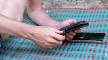 Ormanda Dinlenen Erkek, Renkli Battaniye Üzerine Bir E-Kitap Okuyor. Kapatın. İnsan eli. Uzayı kopyala Eski püskü bir davada akıllı telefon. Kumsal. Hafta sonu. Geçmişi. Açık havada. Vücut parçası.