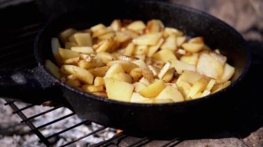 Ormandaki bir kamp ateşinde, Iron Frying Pan 'da kızarmış patates pişirmek. Gün batımında kömürün üstünde dumanlı çıtır patates parçaları. Yemek kavramı, doğada piknik eğlencesi..