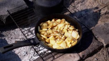 Ormandaki bir kamp ateşinde, Iron Frying Pan 'da kızarmış patates pişirmek. Gün batımında kömürün üstünde dumanlı çıtır patates parçaları. Yemek kavramı, doğada piknik eğlencesi..