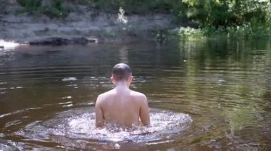 Mutlu Çocuk Gölde Yüzüyor, Güneşin batışında Suyun Altında Dalıyor. Arkadan bak. Sıçramalar, nehirde parlayan güneşin yansıması. Yaz tatilinde açık hava eğlencesi. Tanımlanamaz.