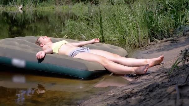 睡梦中的女孩日光浴在湿沙湖畔的一个气垫上 女人仰面躺着 胳膊和腿伸展着 在森林里的大自然中休息 日落了露营 — 图库视频影像