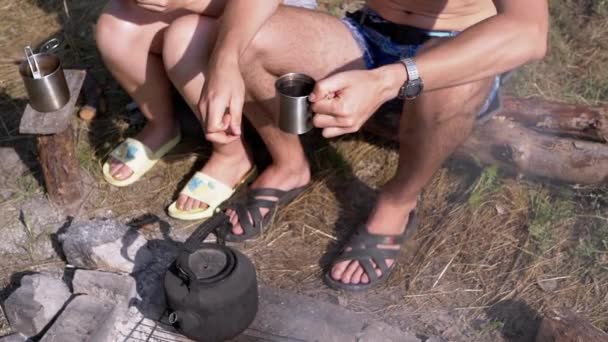 愛のカップルは森の喫煙キャンプファイヤーの近くのマグでホットコーヒーを飲みます 2人を発見する メタルマグ ブラックティーポット 火の近くの森の中の居心地の良い雰囲気 キャンプ リラックス サンセット 晴れた日 — ストック動画