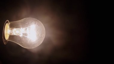 Siyah Arkaplanda Kalın Duman 'da Parlayan Bir Yanan Ampul. Yan görüş. Tozlu, açık Edison tungsten ampulü dumanlı karanlık odada sarı bir ışık parlıyor. Bulanık hareket. Doku. Sis.