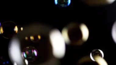 Renkli sabun köpükleri ıssız Kara Arkaplanda, boşlukta uçuyor. Renkli ışıklar. Birçok gökkuşağı şeffaf kabarcıkları rastgele döner, yüzer, düşer, patlar. Spot. Bulanık hareket. Odaklan. Soyut.